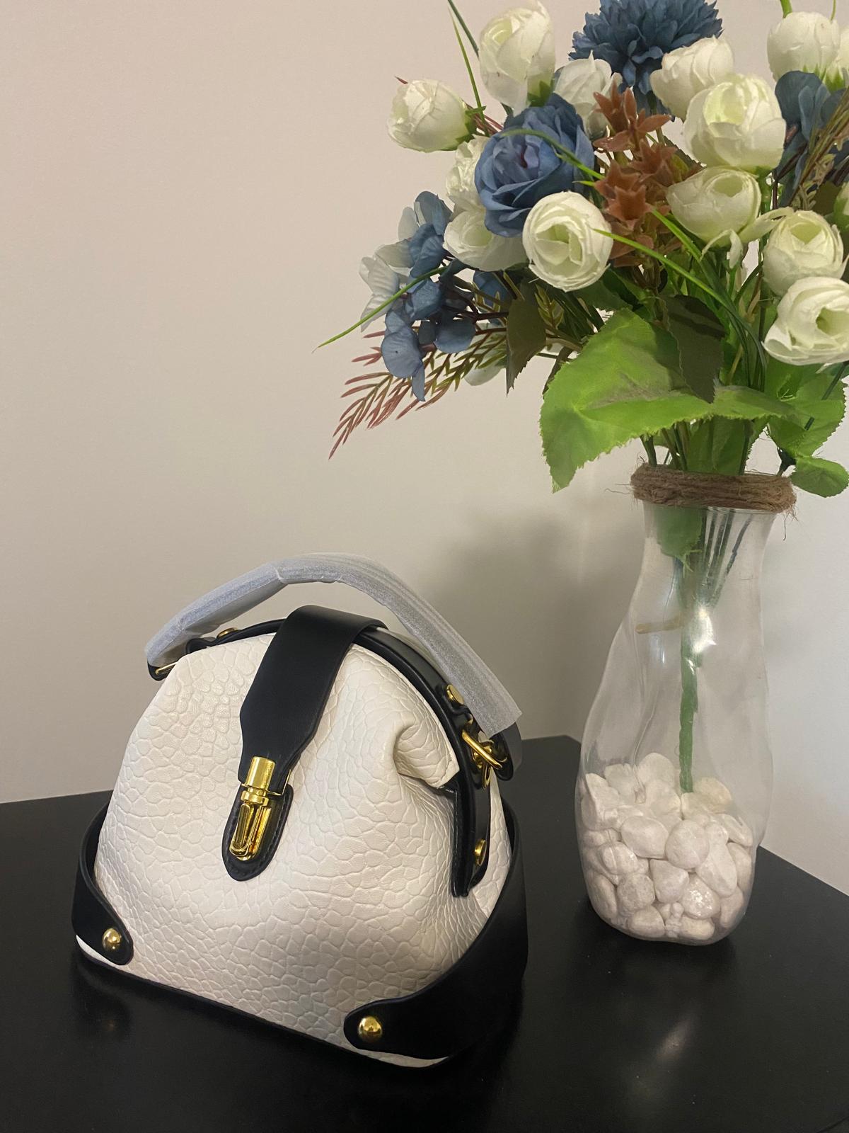 A structured, white-textured leather handbag with black trim and gold-tone hardware.