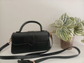 A black faux-leather handbag with a top handle and detachable shoulder strap,