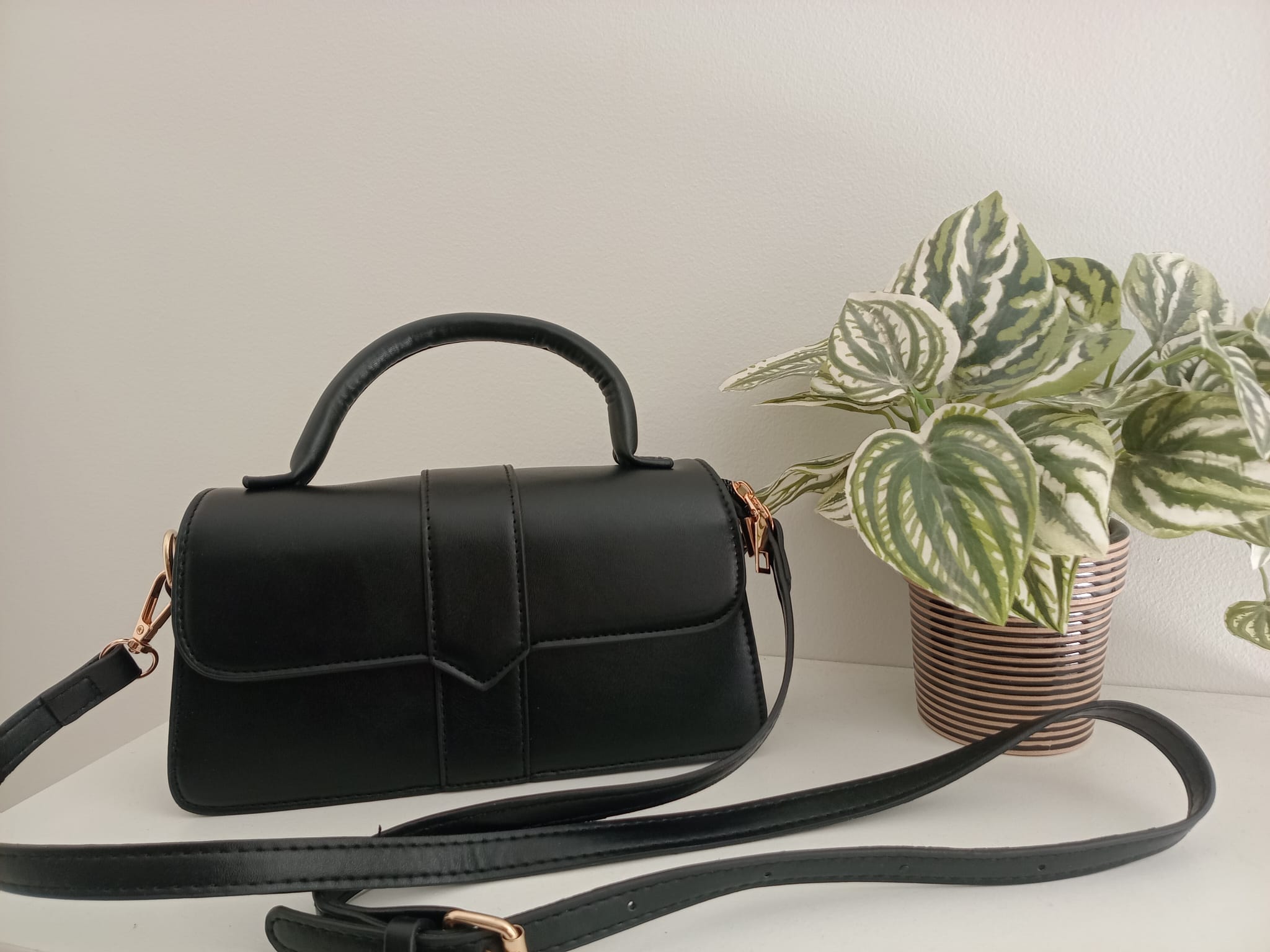 A black faux-leather handbag with a top handle and detachable shoulder strap,